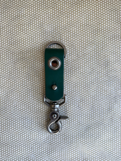 Green leather keychain with metal clasp on a textured beige background