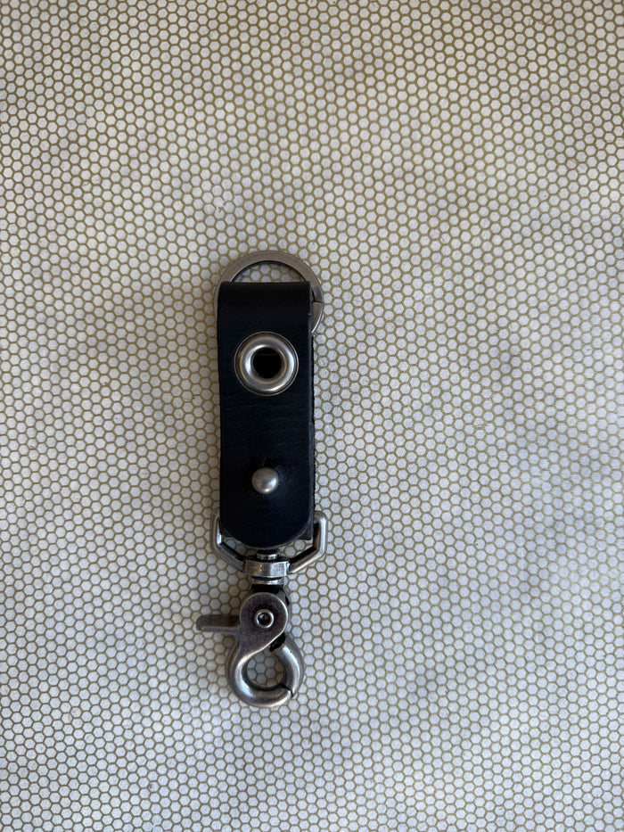Black leather key fob with metal clip on a textured beige background