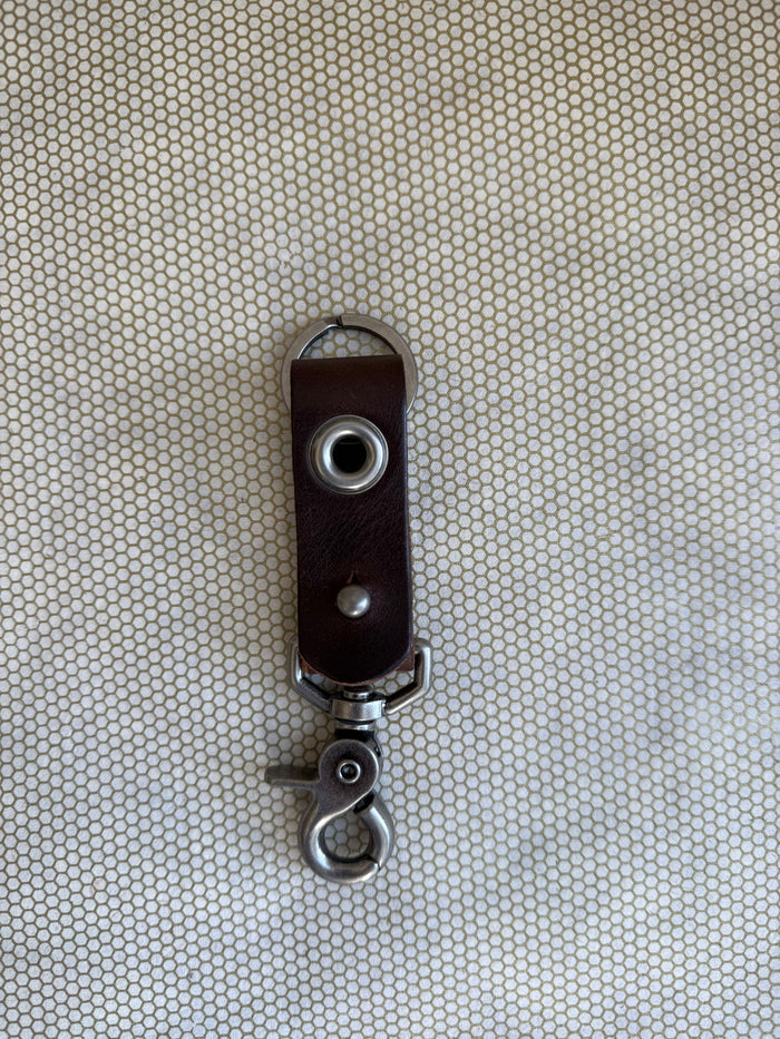 Brown leather key fob with metal clip on a textured beige background