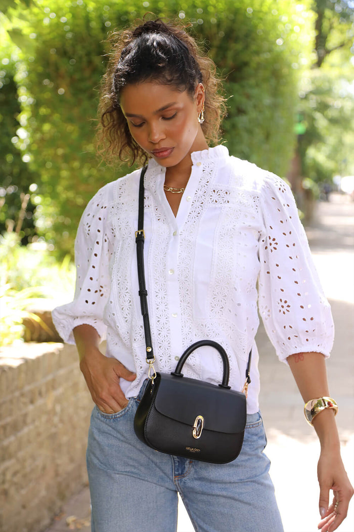 Female model wearing the  Delia Black faux leather Top Handle Crossbody across her body with the crossbody strap attached