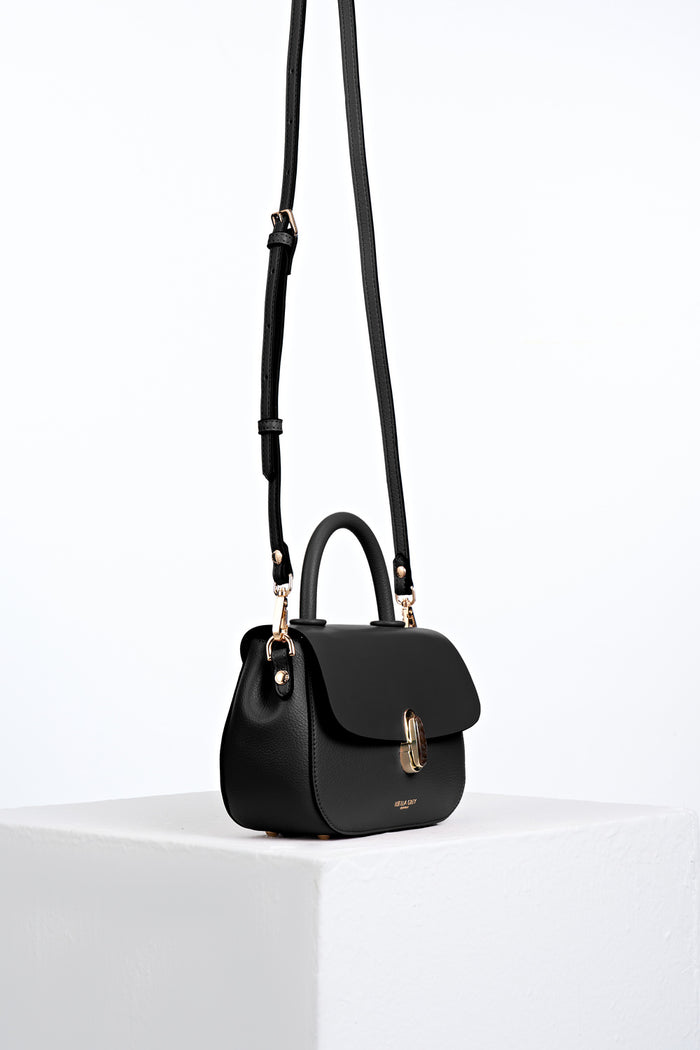Side view of the  Delia Black faux leather Top Handle Crossbody with the crossbody handles attached to the gold hoops on the bag's side