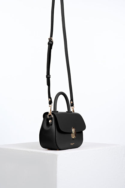 Side view of the  Delia Black faux leather Top Handle Crossbody with the crossbody handles attached to the gold hoops on the bag's side