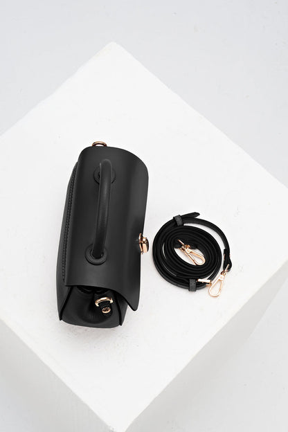 Overhead view of Delia Black faux leather Top Handle Crossbody showing the top grab handle and the detachable crossbody strap rolled up beside the bag