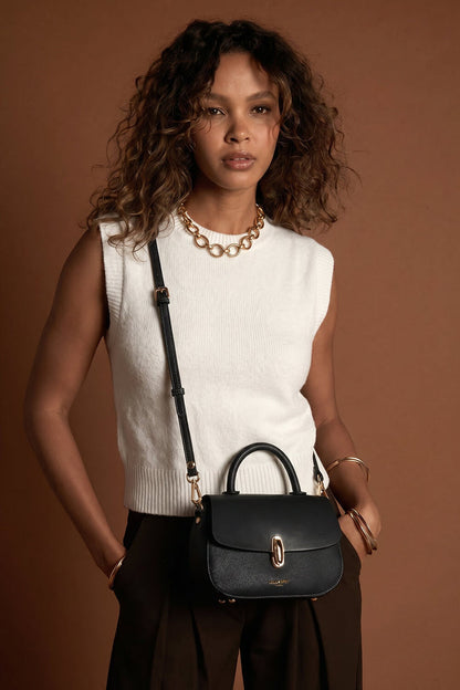 Female model wearing the Delia Black faux leather Top Handle Crossbody across her body using the crossbody strap