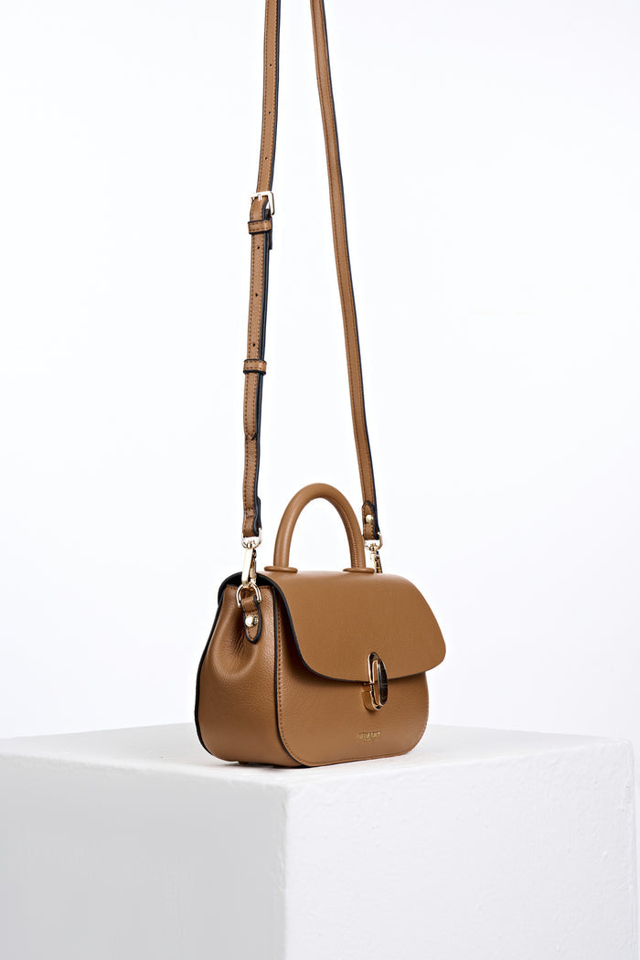 Side view of the  Delia Tan faux leather Top Handle Crossbody with the crossbody handles attached to the gold hoops on the bag's side
