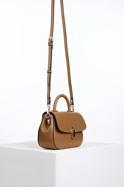 Side view of the  Delia Tan faux leather Top Handle Crossbody with the crossbody handles attached to the gold hoops on the bag's side