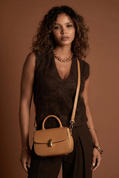 Female model wearing the Delia Tan faux leather Top Handle Crossbody across her body using the crossbody strap