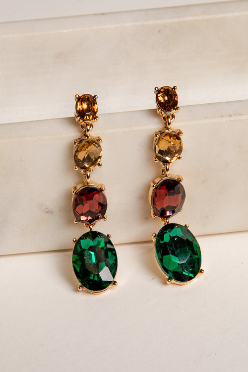Pair of gold earrings with green and red gemstones on a light background