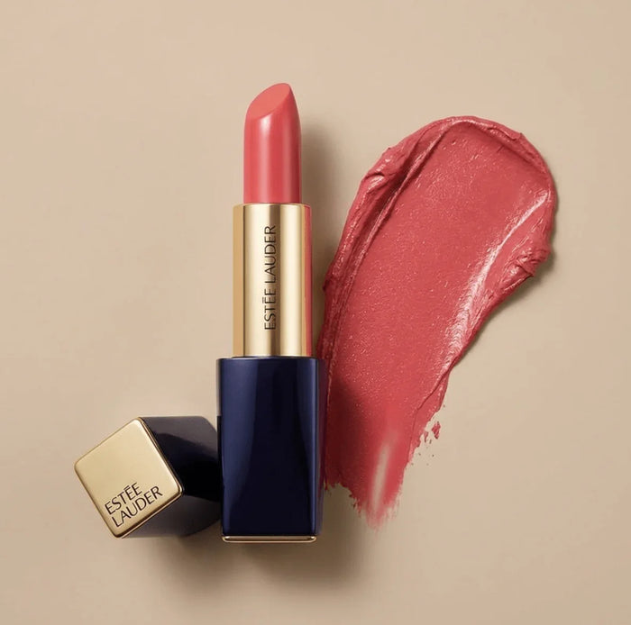 Matte pink lipstick in gold and navy case with matching lipstick swatch on beige background.
