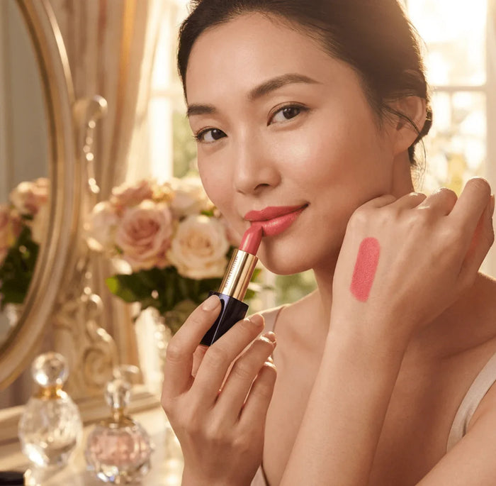Woman applying pink matte lipstick, lipstick swatch on hand, elegant vanity background
