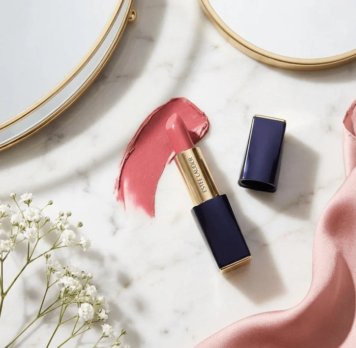 Matte pink lipstick on marble with swatch, gold and navy tube, and decorative accents
