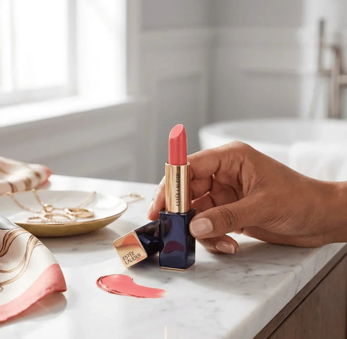 Hand holding pink matte lipstick on marble vanity with gold accents and smeared swatch