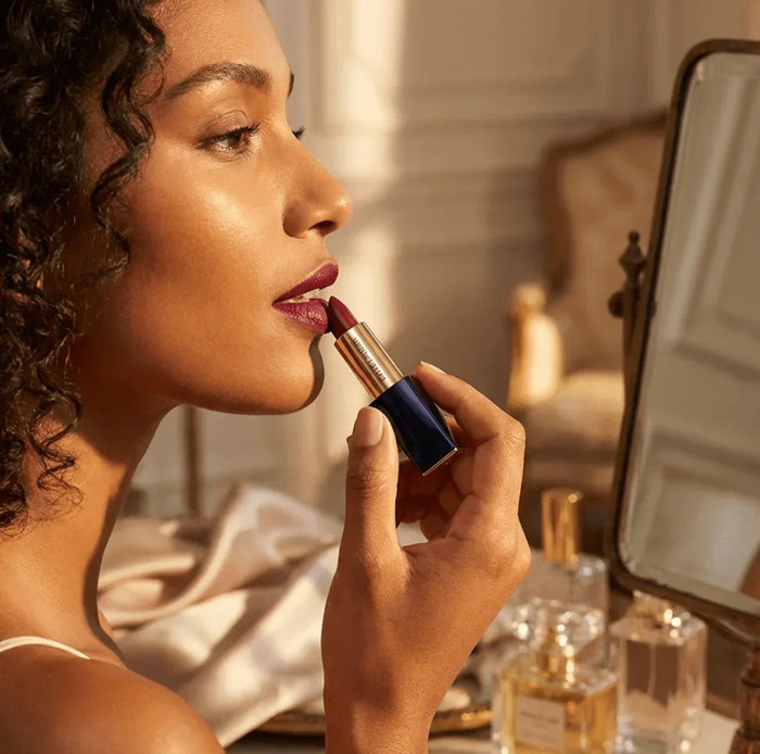 Woman applying matte dark red lipstick in front of a mirror, beauty makeup scene