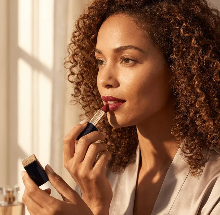 Woman applying matte red lipstick, close-up, natural indoor lighting, beauty product focus