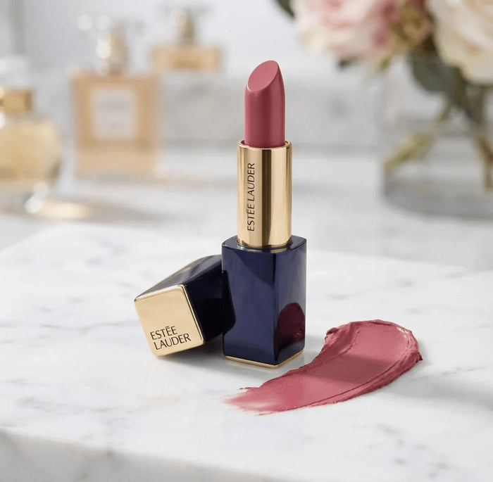 Pink mauve Estee Lauder lipstick with gold and navy case on marble, lipstick smear beside.