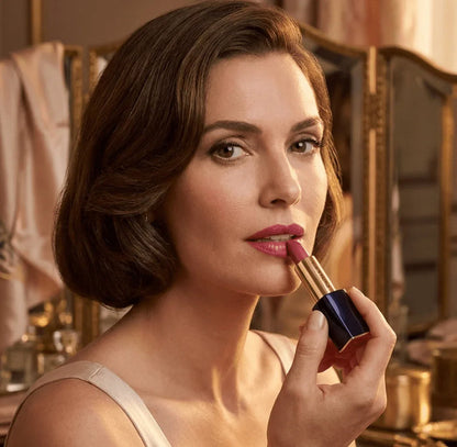 Woman applying pink sculpting lipstick with gold and navy blue case in elegant room