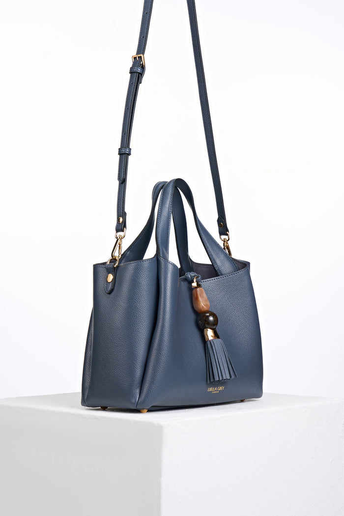 Side view of Etta Denim Blue faux leather Small Tote with detachable crossbody strap attached to the gold rings on the bag's side