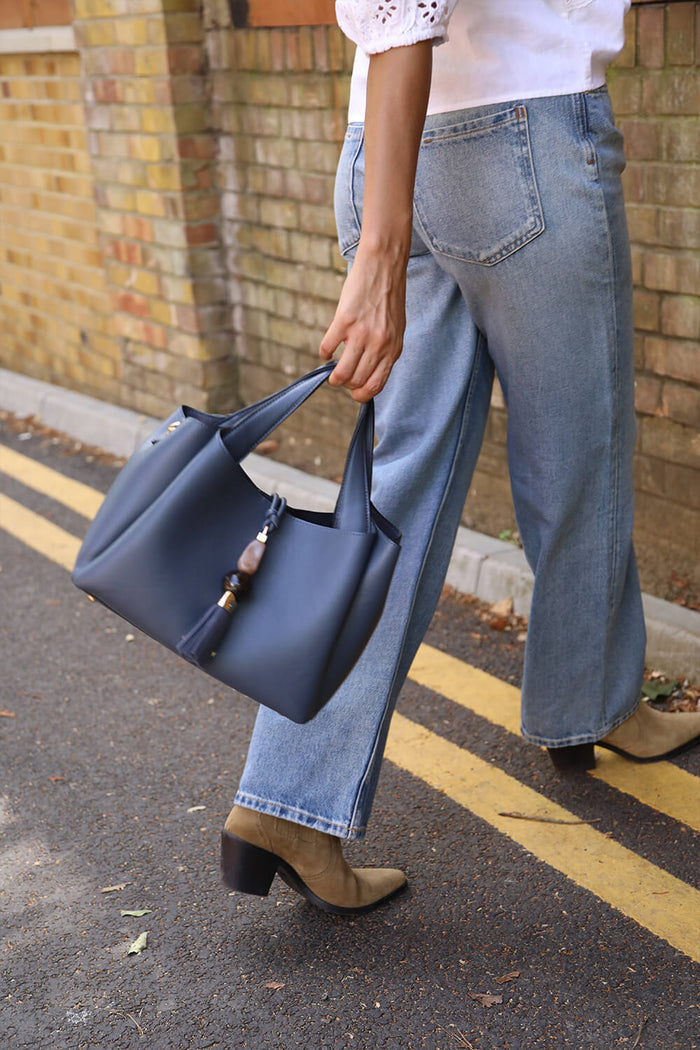 Female model holding the Etta Denim Blue faux leather Small Tote by the top grab handles in her hands