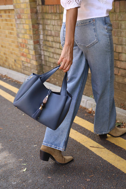 Female model holding the Etta Denim Blue faux leather Small Tote by the top grab handles in her hands