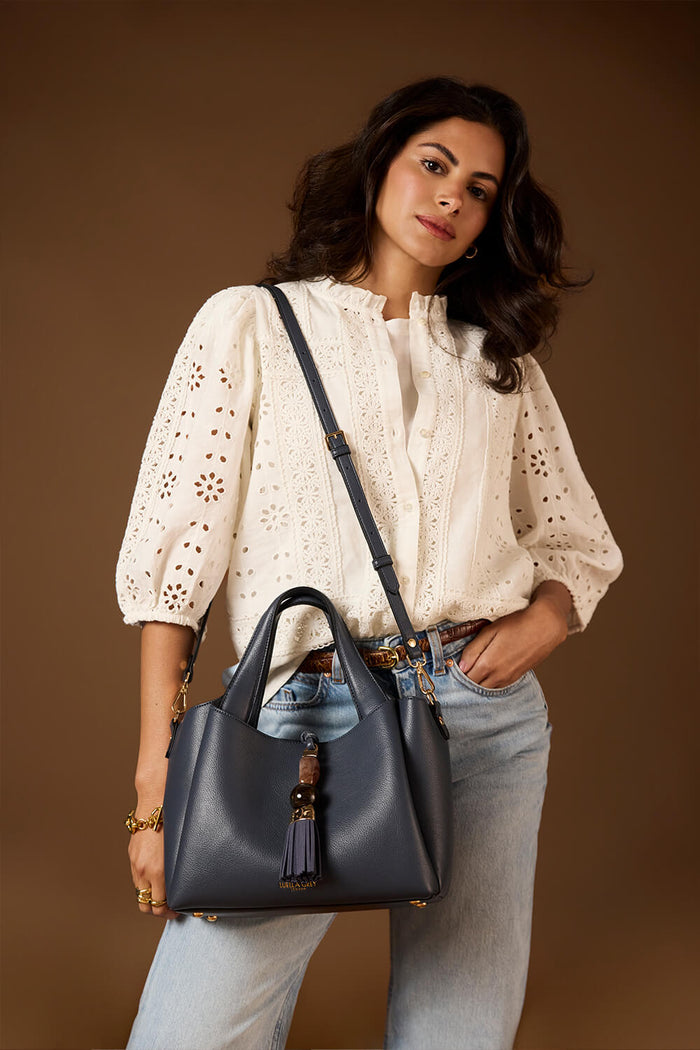 Female model wearing the Etta Denim Blue faux leather Small Tote over her shoulder using the detachable crossbody strap
