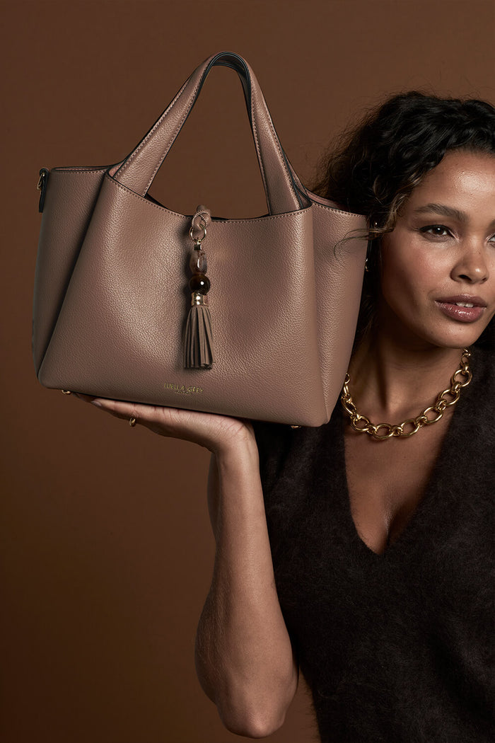 Female model holding Etta Fawn faux leather Small Tote in her hand by the bottom of the bag