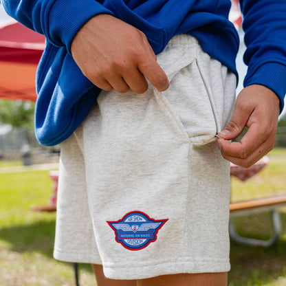 Adult male model in heather gray Fastball Flight sweatshorts demonstrating zip pocket at outdoor baseball event