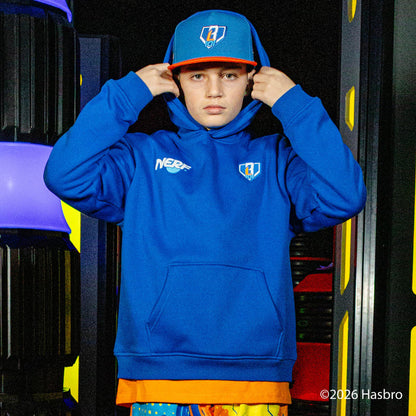 Person wearing a blue hoodie and cap with 'NERF BL101' branding, standing in front of colorful equipment.