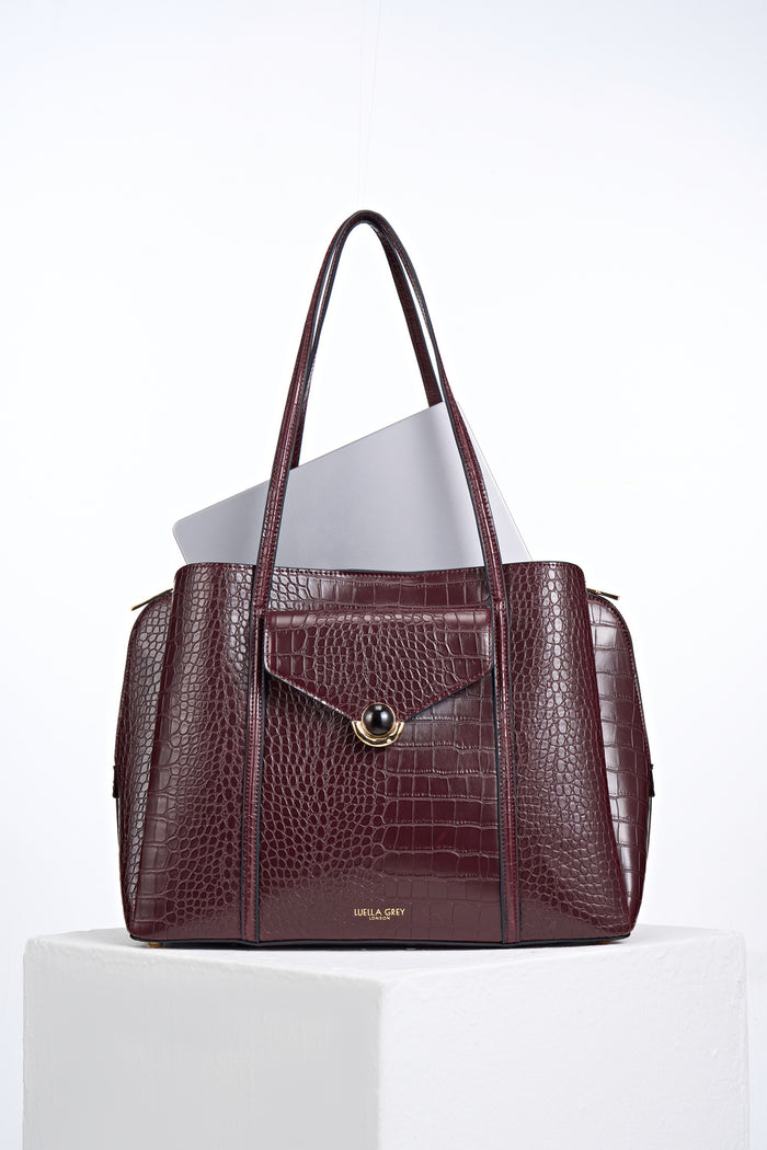 Front view of Francois Black Cherry Crocodile print faux leather Laptop Tote with laptop inside and resin and gold Crystal Palace clasp closure detail on front flap