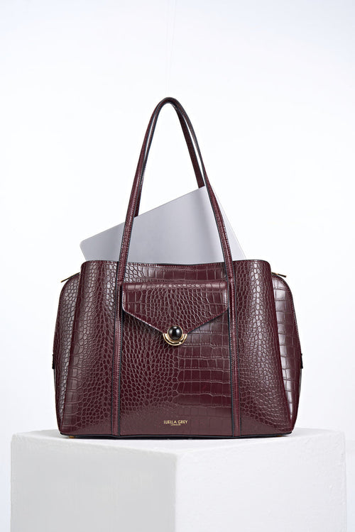 Front view of Francois Black Cherry Crocodile print faux leather Laptop Tote with laptop inside and resin and gold Crystal Palace clasp closure detail on front flap
