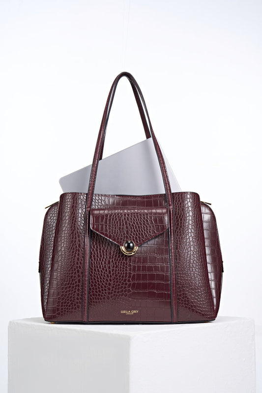 Front view of Francois Black Cherry Crocodile print faux leather Laptop Tote with laptop inside and resin and gold Crystal Palace clasp closure detail on front flap