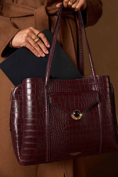 Female model holding the Francois Black Cherry Crocodile print faux leather Laptop Tote by the shoulder straps and putting a laptop into the central laptop zipper compartment