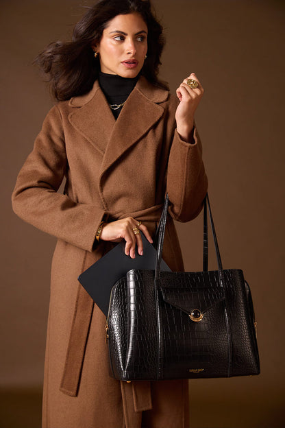 Female model holding the Francois Black Crocodile print faux leather Laptop Tote by the shoulder straps and putting a laptop into the central laptop zipper compartment