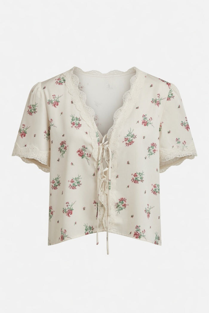 An off-white short-sleeve blouse with a delicate pink and green floral print, featuring a lace-trimmed V-neckline and front tie closure, shown against a plain white background.