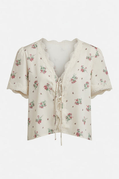 An off-white short-sleeve blouse with a delicate pink and green floral print, featuring a lace-trimmed V-neckline and front tie closure, shown against a plain white background.