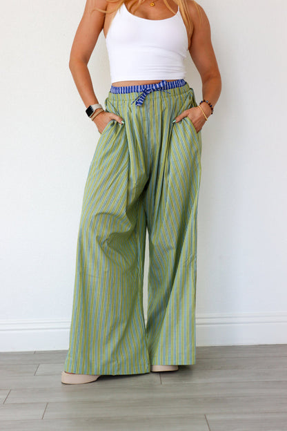 Person wearing green striped wide-leg pants and a white top against a white wall.