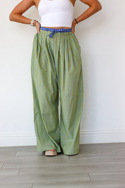 Person wearing green striped pants and a white top against a plain background