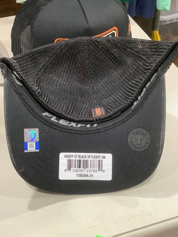Black Flexfit trucker hat with a mesh back, shown from the inside of the brim with a product label and Flexfit branding visible.