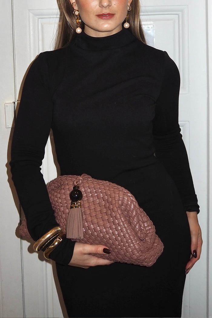 Woman holding a pink woven clutch bag against a white background