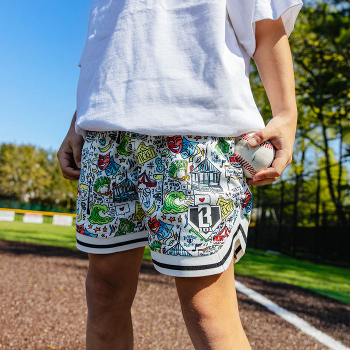 Close-up of the youth white Jackson Olson x BL101 Hometown Shorts showing the all-over illustrated print, BL101 home plate logo, and striped hem