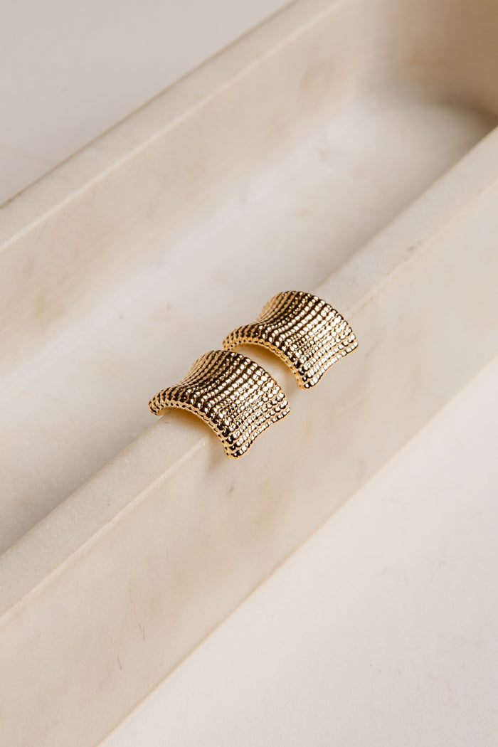 Gold textured earrings on a light wooden surface