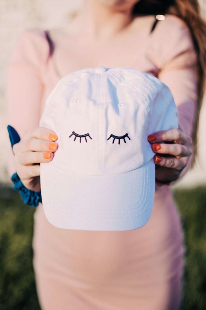 white baseball cap with black eyelashes stitched on