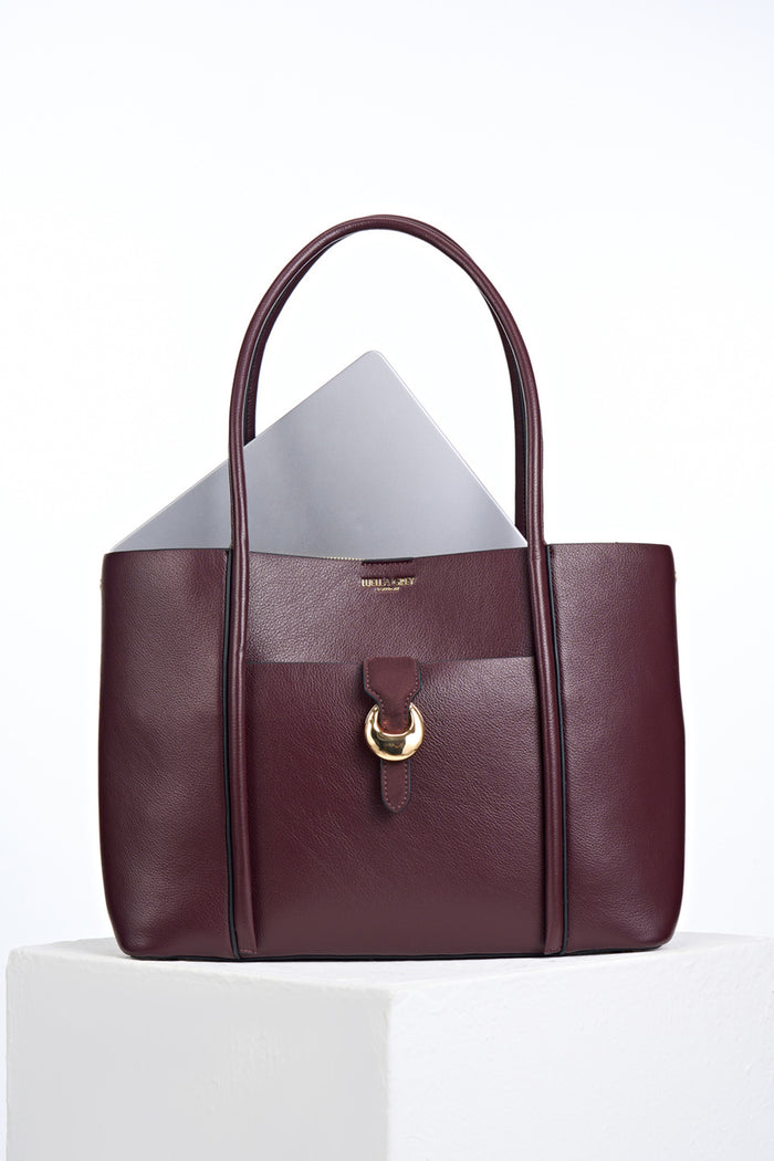 Front of Lilibet Black Cherry faux leather Laptop Tote with a laptop in the top showing molten metal Cannon Street Clasp closure on front slip-in pocket