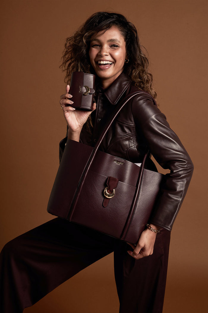 Female model wearing Lilibet Black Cherry faux leather Laptop Tote over her shoulder using the shoulder straps and holding matching Letitia Black Cherry Medium Purse