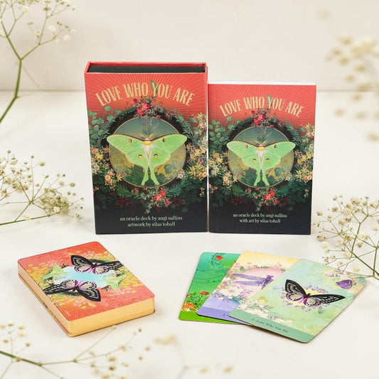 Two oracle decks titled 'Love Who You Are' with butterfly illustrations on a white surface with flowers.