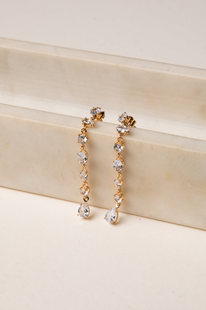 Gold and crystal drop earrings on a beige surface