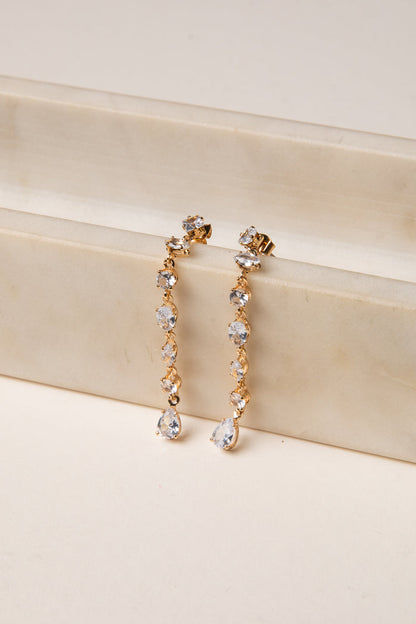 Gold and crystal drop earrings on a beige surface