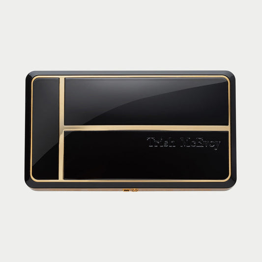 Black and gold compact mirror with 'Trish McEvoy' branding on a light gray background