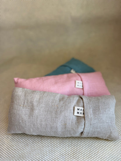 Three stacked eye pillow cushions in pink, gray, and blue on a textured surface.