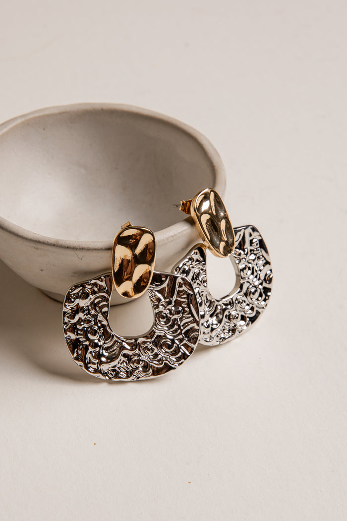 Gold and silver hoop earrings on a white surface with a neutral background