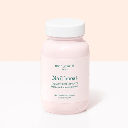 A pink bottle labeled Manucurist Nail Boost contains 60 nail supplement capsules for a 1-month routine, designed to strengthen and speed nail growth. Features a white cap and is set against a light pink and white background.